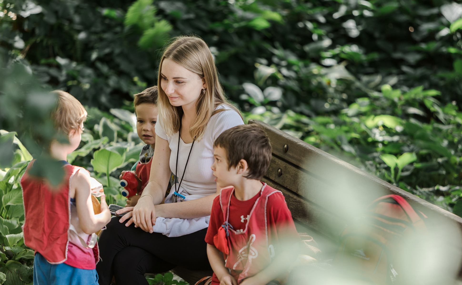 Teacher and three children talk together surrounded by trees.